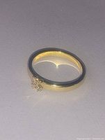 Close-up front view of gold plated ring with small gemstone cluster in 'K' shape.