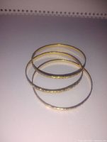 Three gold plated bangles stacked together showing smooth and textured designs.