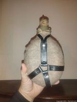 Front view of vintage military canteen with wool cover and leather straps held in hand.