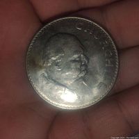Close-up photo of 1965 English Winston Churchill Crown coin showing detailed side profile and inscription 'CHURCHILL'. Coin dimension approximately 1.7 inch diameter.