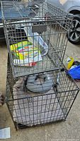 two stacked black wire dog crates with towel and inflatable collar inside