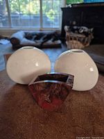 Two white ceramic Crate & Barrel bud vases and one red-brown stone bud vase displayed together