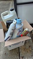 Box containing two white jugs, Lysol Laundry Sanitizer, aerosol stain remover, black cylindrical cleaner, Wenol metal polish tube