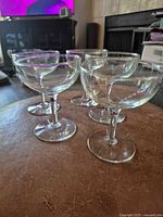 Five clear glass champagne coupes on table, angled view
