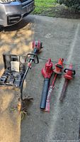 Group of four red yard tools on driveway: string trimmer, leaf blower, two hedge trimmers