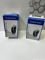 Two boxed portable electric wall-mounted heaters displayed upright showing minor damages to the boxes.