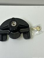 Front view of black cast metal trailer coupler lock and two keys in plastic bag.