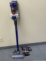 Front view of assembled vacuum and loose attachments displayed on floor against wall