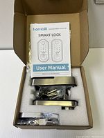 Smart lock components including user manual, exterior and interior lock units, keys, USB cable, silica gel packet in foam packaging within cardboard box.