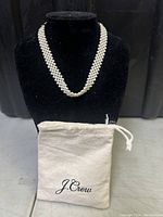 Front view of the woven faux pearl choker necklace displayed on black stand with J.Crew branded cream drawstring pouch in front.