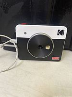Front view of the Kodak Mini Shot C300R instant print camera showing lens, branding, and USB cable