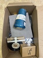 View from top of cardboard box showing a large spool of turquoise yarn, some vintage vinyl records, grey fabric, and cardboard boxes.