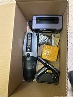 Top view of box showing handheld vacuum, grey electronic device, small bags with parts and yellow packaged item