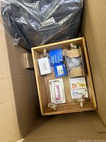 Top-down view of wooden tray containing various small items including a pink nail clipper, a box labeled 'Care for Calluses', and other packaged items