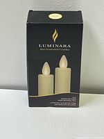 Front view of packaging showing two ivory taper candles with flame effect image and Luminara branding