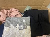 Box of mixed clothing pieces including pink and black items, and a white/gray striped zip-up hoodie, showing general contents of clothing in small and extra small sizes.