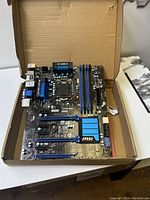 MSI Z77A-G45 motherboard placed inside a cardboard box, showing the layout and components including blue heatsinks, RAM slots, PCIe slots, and ports.
