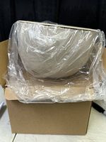 Side view of round beige Kinto plant pot in plastic wrap, inside cardboard box.