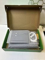 Opened box showing folded grey grounding sheet with snap buttons and white cord inside plastic packaging.