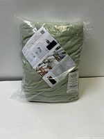 Packaged sage green tablecloth with included information sheet showing example usage.