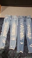 Two pairs of light blue distressed American Eagle jeans laid flat. Both show heavy front distressing and ripped details. One pair slightly longer than the other.