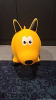 Front view of the yellow dog-shaped animal hopper toy showing cartoon eyes, nose, ears, and body shape