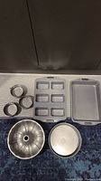 Photo showing entire bakeware set including several pans and rings on carpeted floor and white mat.