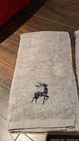 Beige hand towel showing black embroidered reindeer with white dots