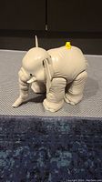 Side view of the Fisher Price Little People elephant toy on a blue surface, showing the moving legs, body structure, and a small yellow figure on its back.