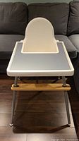 Front view of Ikea high chair with customized blue placemat on tray, showing clean white seat and metal legs on wood floor.