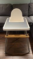 Front view of Ikea high chair with gray placemat and wooden leg rest on dark floor.