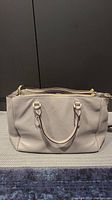 Front view of large gray leather Kate Spade purse with two carrying handles and gold hardware.