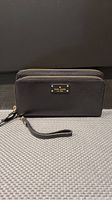Front of the black Kate Spade wallet wristlet showing logo plaque and zipper.