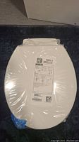 Top view of white Kohler toilet seat sealed in original clear plastic packaging showing the label with model number 1394504-0 and instructions.