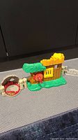Green treehouse playset with yellow shutters and target, connected to a small fenced area.