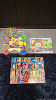 Photo showing three wooden educational toys: a bead maze, a fire station puzzle, and an alphabet puzzle board