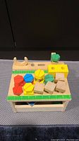 Front view of the wooden toy tool bench showing colorful wooden screws, nuts, and blocks on top along with the wooden wrench and ruler surface.