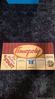 Top view of the folded game board featuring the Timopoly logo and Tim Hortons-themed properties such as 'Breakfast Sandwich Blvd', 'Iced Capp Cres', and 'Regional Marketing'.