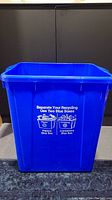 Front view of tall blue plastic recycling bin with printed recycling instructions on the side.
