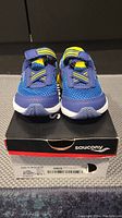 Front view of blue and yellow Saucony kids shoes on original Saucony box showing mesh upper and hook-and-loop strap.