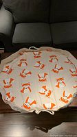 Round fabric play mat laid flat displaying orange and white fox face pattern.