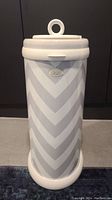 Front view of the grey and white chevron patterned metal diaper pail with Ubbi logo and circular lid handle.