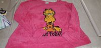 Front view of a pink fluffy long sleeve shirt featuring a graphic of Garfield covering his eyes with the phrase 'Not Today' underneath.