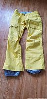 Front view showing yellow snowboarding pants with flap pockets, buttons, and adjustable waist.