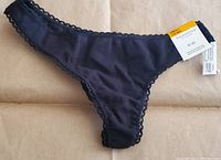 Front view of black thong underwear with lace trim and price tag showing size small and brand Charter Club.