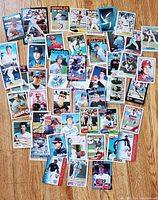 Photo showing about 30+ vintage baseball cards spread on a wooden floor with various major league players visible in uniforms from the 70s, 80s, and 90s.