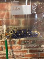 Chunky blue and gold bead necklaces inside a clear plastic Ziploc bag against brick background.