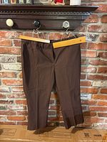 Dark brown women's dress pants size 16 by Lane Bryant hanging on wooden hanger against brick wall.
