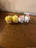 Four windup toys - two yellow fluffy chicks and two white fluffy bunnies with pink ears, sitting on a wooden surface.