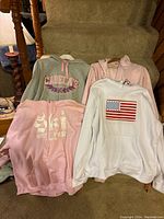 Four sweatshirts laid out on a carpeted staircase, showing two hoodies and two sweatshirts with visible logos and graphics.